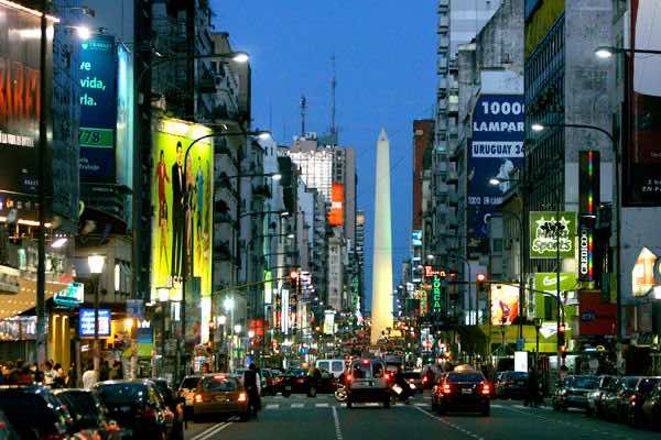 Avenida Corrientes iluminada: libros, neón, tránsito humano y un Obelisco que vigila. Buenos Aires, entre el vértigo y la resistencia.